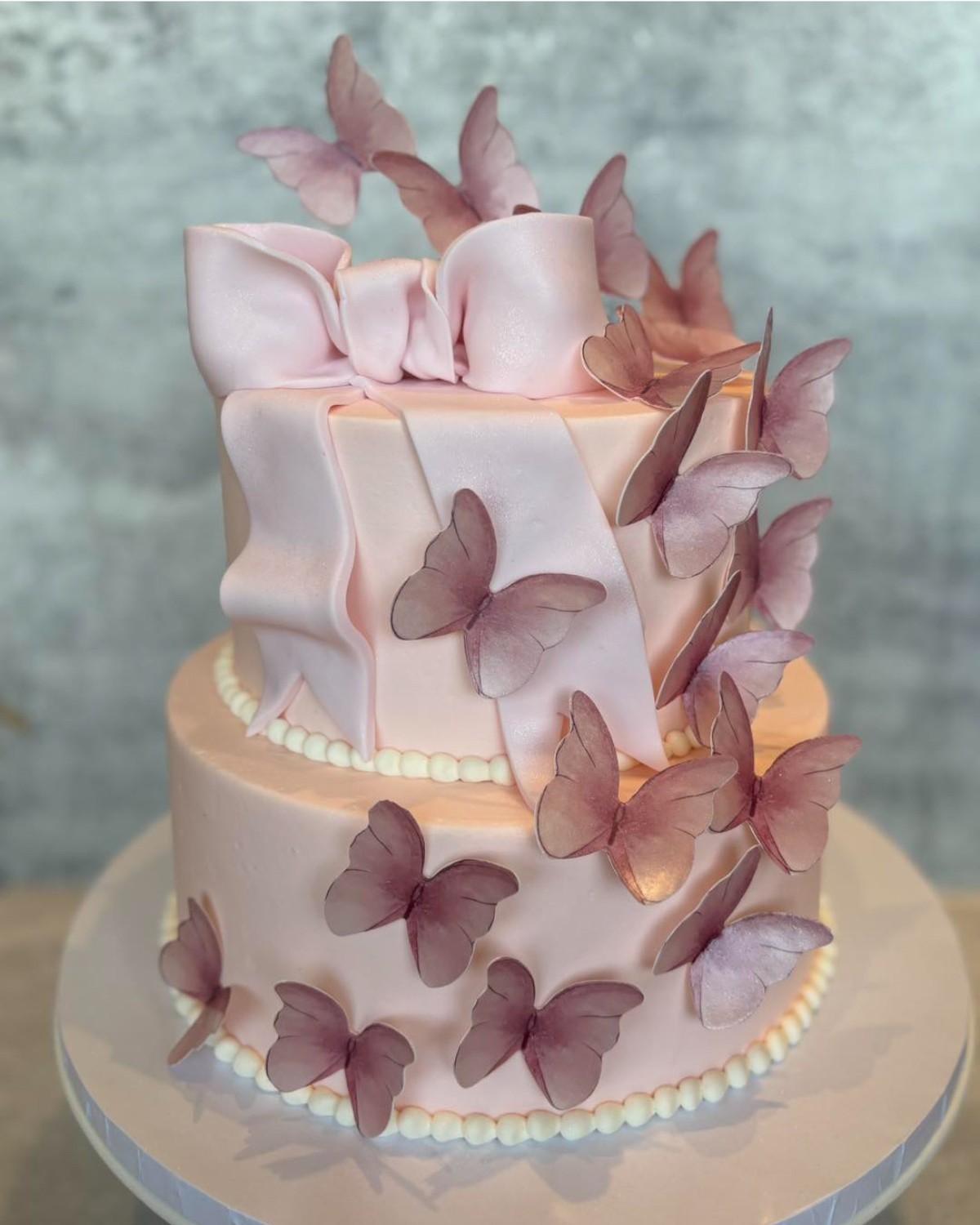 Two-tier pink cake with fondant bow and purple butterflies