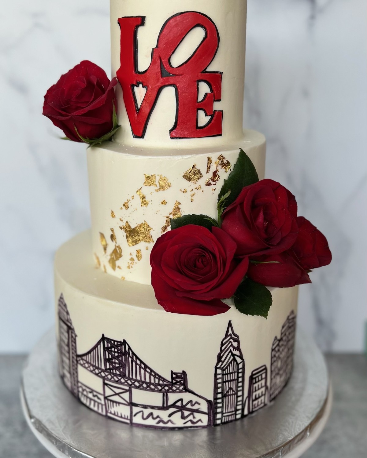 Three-tier city skyline wedding cake with red roses and gold leaf